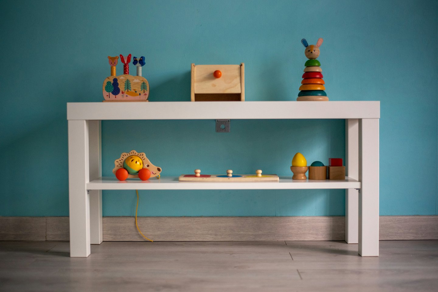 Bunte Holzspielzeuge für Kinder, ordentlich auf einem türkisfarbenen Wandregal arrangiert.