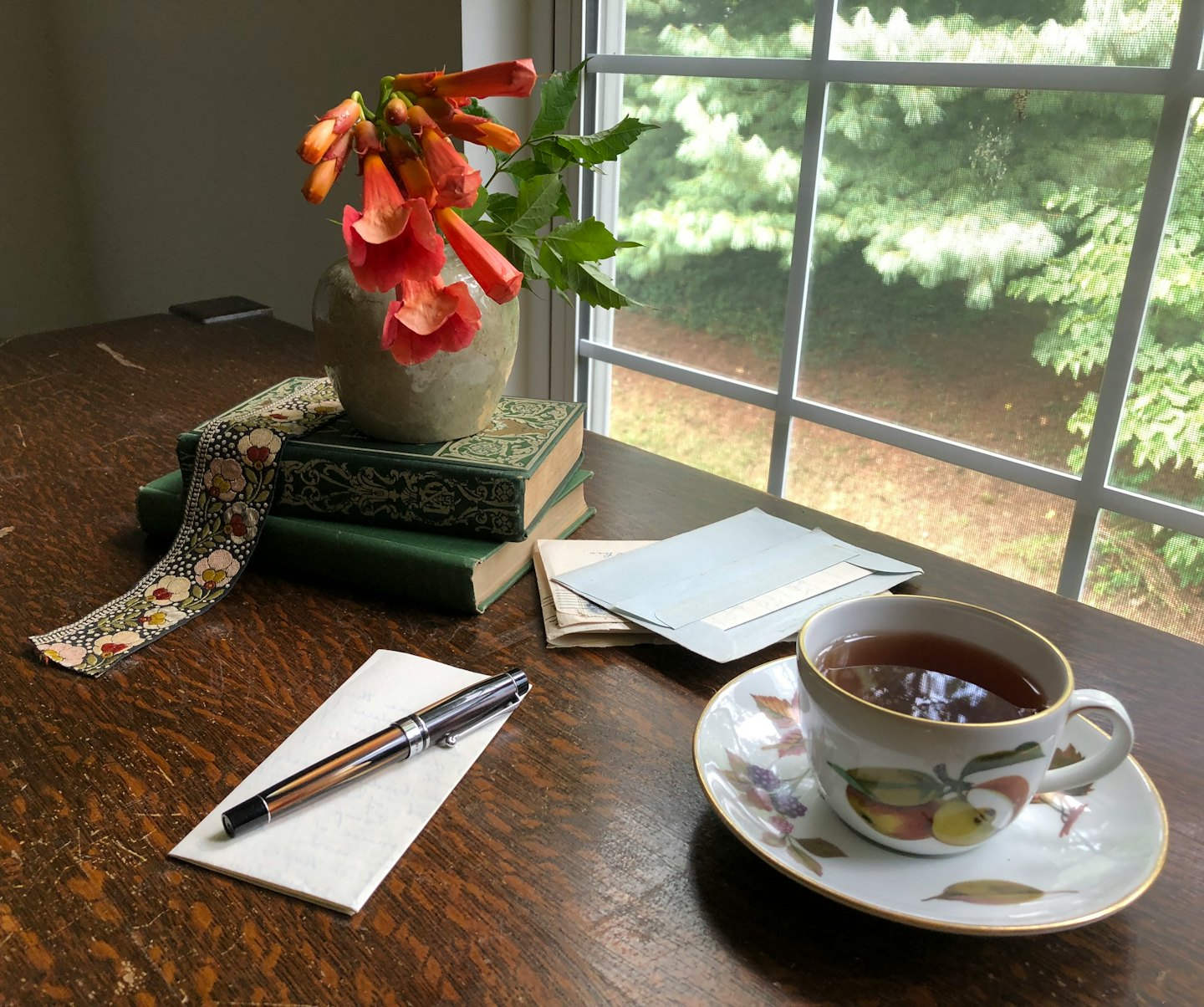 Schreibtisch mit Büchern, Blumen und einem Füllfederhalter.