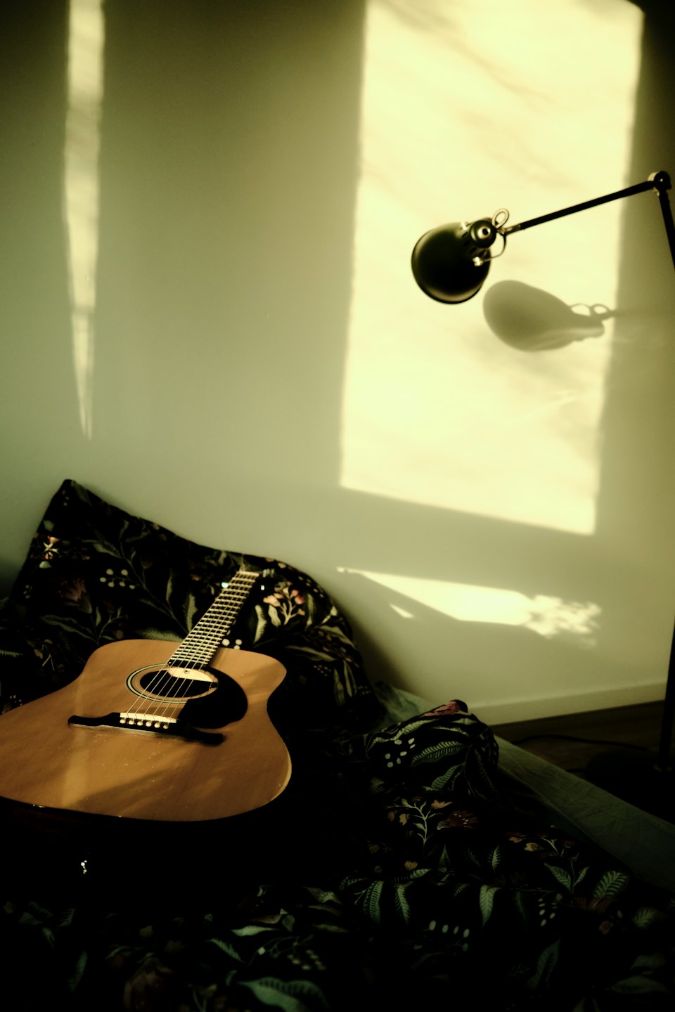 Akustikgitarre lehnt an einer Wand auf einem floralen Kissen.