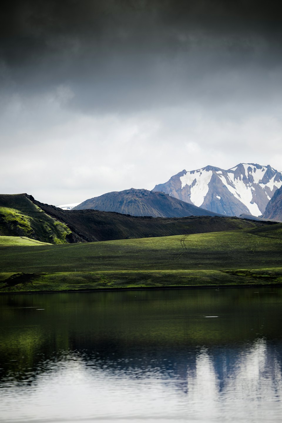 Schneebedeckte Berge erheben sich über einem stillen See und grünen Hügeln.